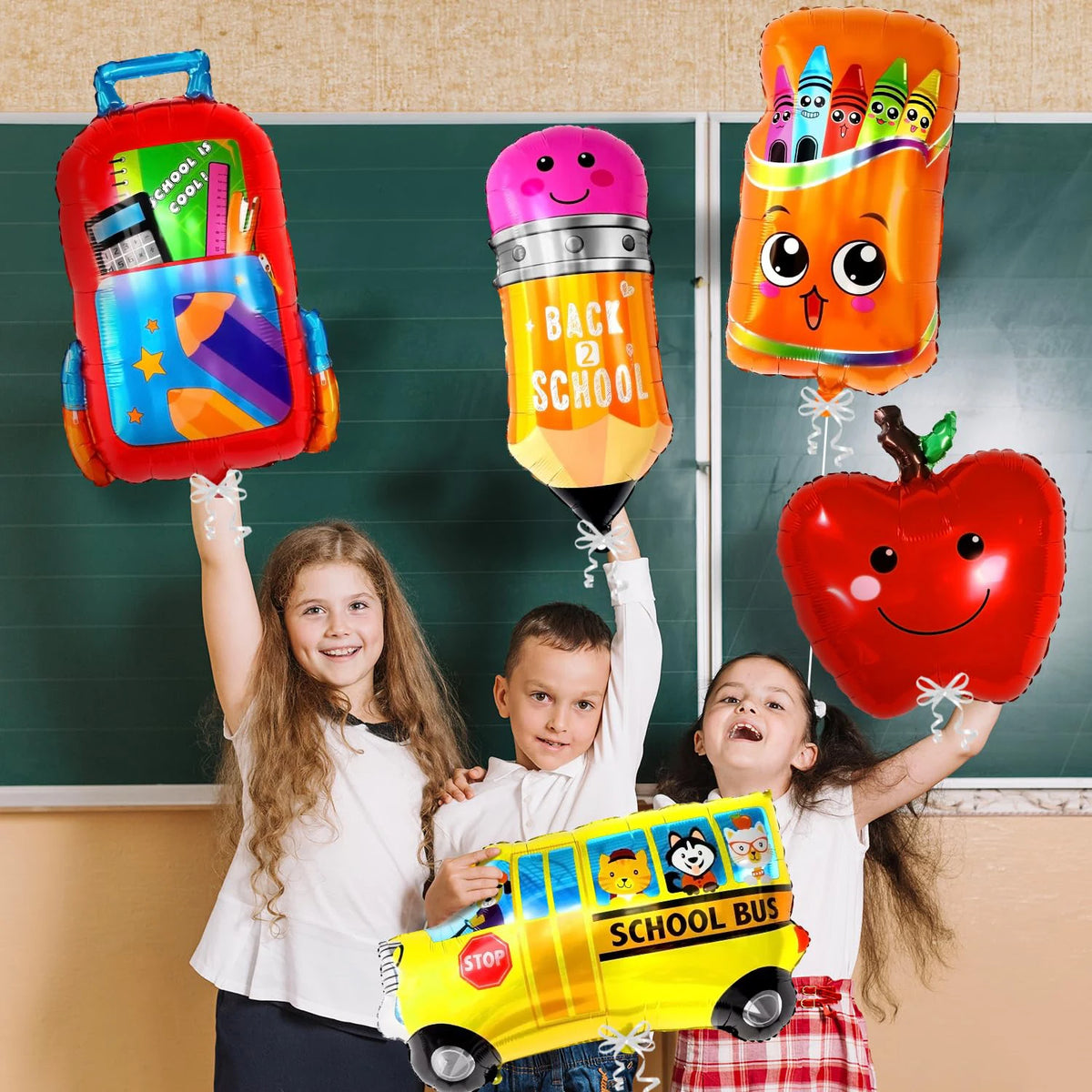 A group of children holding a large orange school bus foil balloon and an apple in front of a chalkboard.