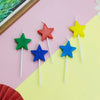 A collection of colorful star-shaped birthday cake candles in red, yellow, green, and blue against a pink and yellow backgrou