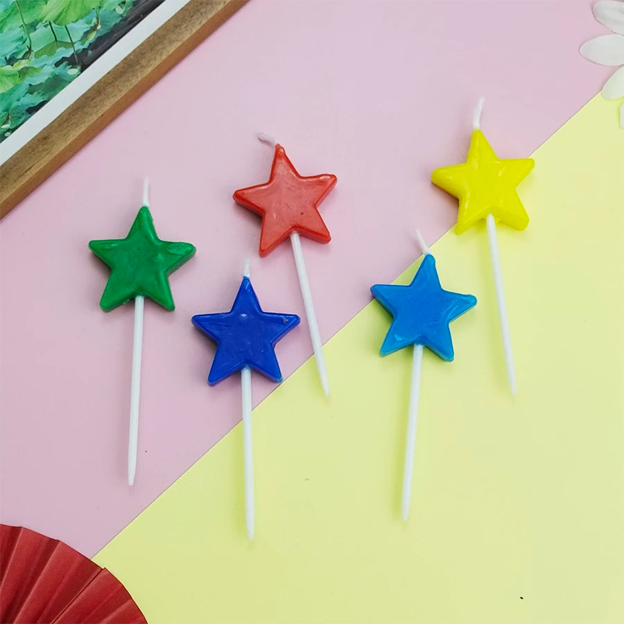A collection of colorful star-shaped birthday cake candles in red, yellow, green, and blue against a pink and yellow backgrou