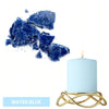 A light blue candle in a gold wire holder next to vibrant water blue dye blocks.