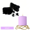 A purple candle in a gold wire holder next to black dye blocks.