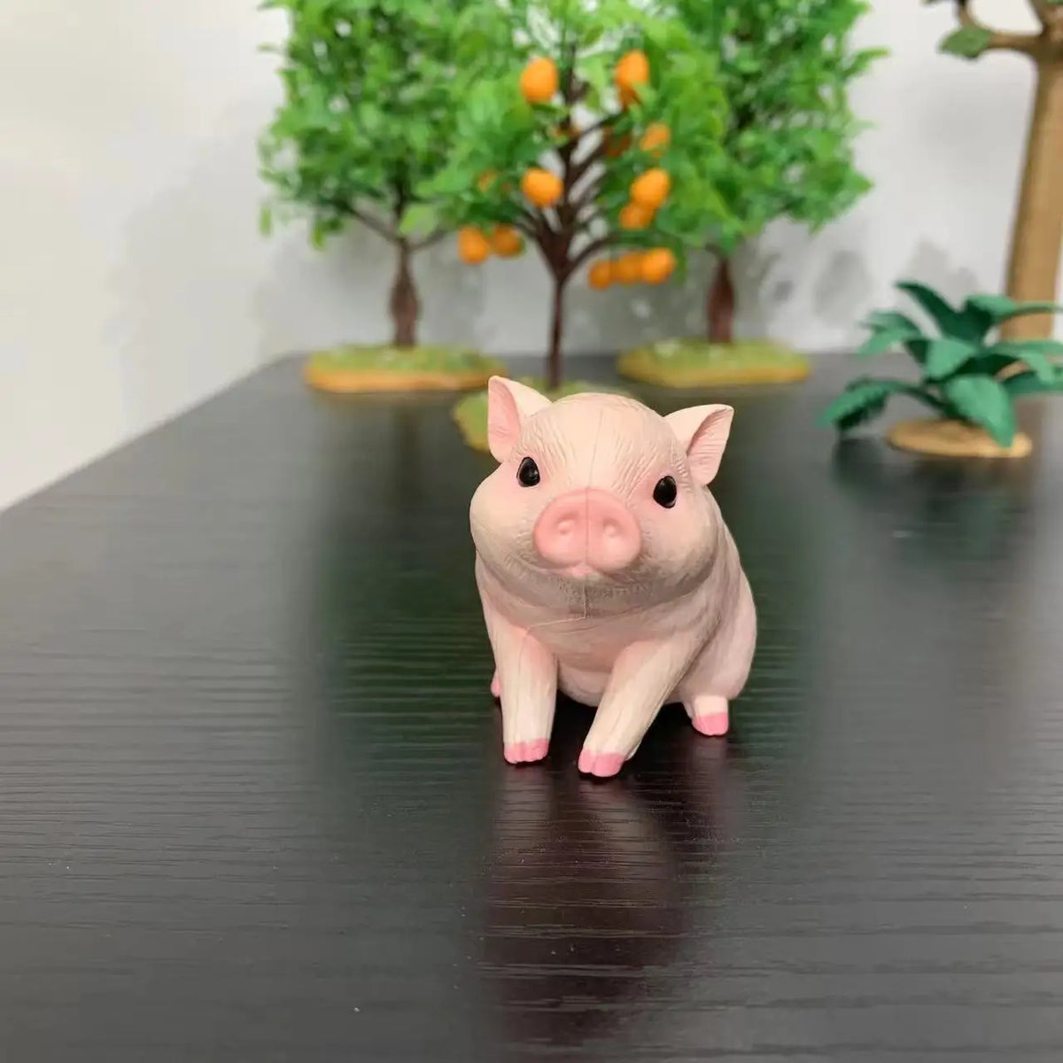 A small, pink pig figurine is displayed in front of a background featuring green trees with orange fruit.