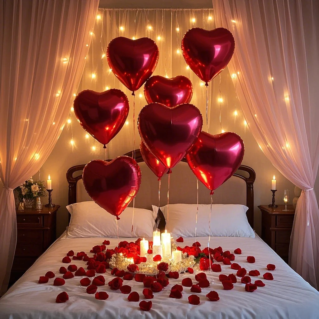 A bed decorated with red rose petals and heart-shaped foil balloons in a romantic setting.