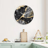 A round black marble textured glass wall clock with gold accents hanging on a white wall.
