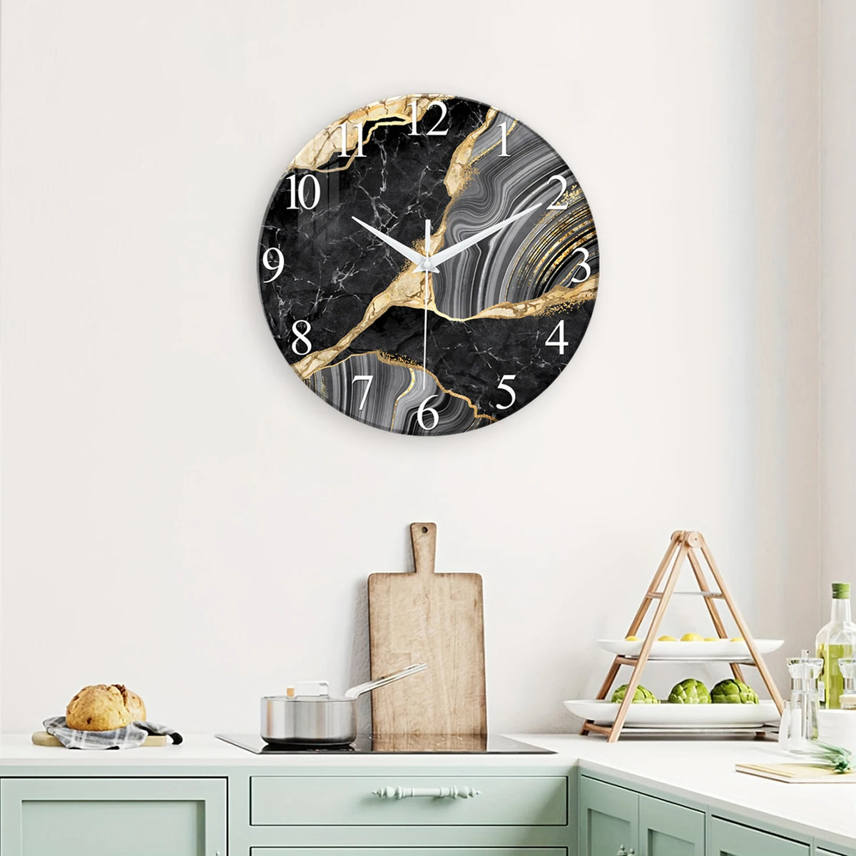 A round black marble textured glass wall clock with gold accents hanging on a white wall.