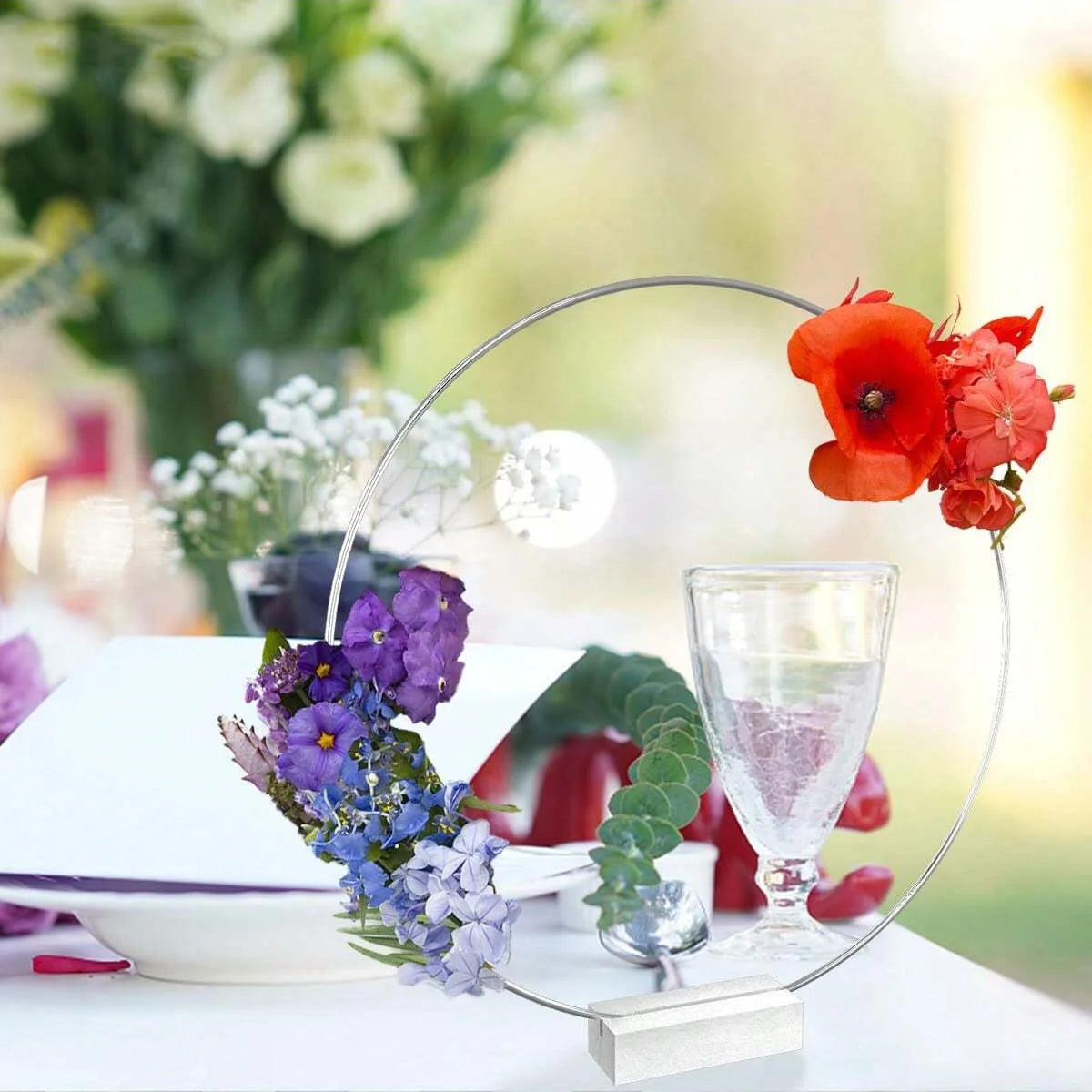 A set of ten gold metal hoop centerpieces with stands featuring floral arrangements and a glass.