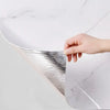 A hand is peeling off a silver marble pattern self-adhesive wallpaper from a white marble surface.