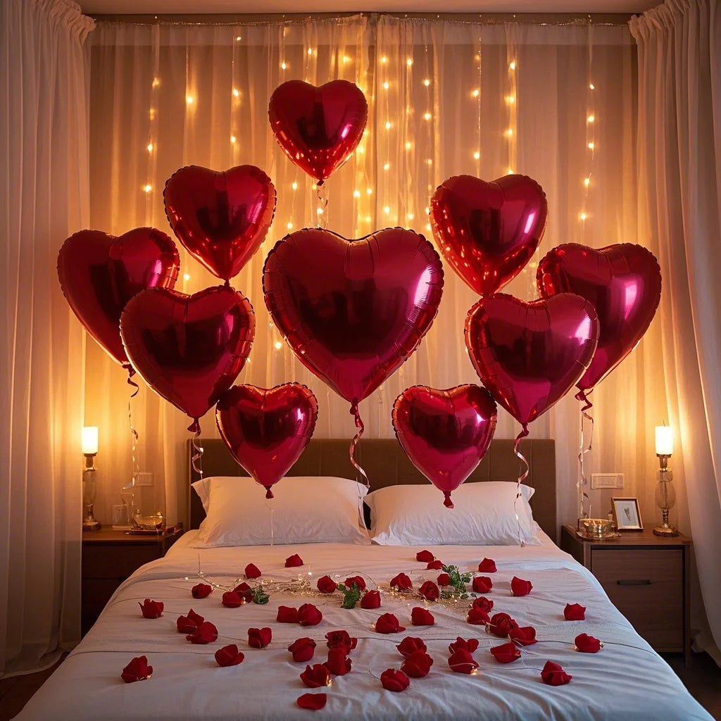 A bed decorated with red rose petals and heart-shaped foil balloons in various shades of pink and red.