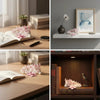 A collection of delicate pink cherry blossom flowers and a miniature figurine displayed on a wooden table.