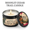 A jar of Moonlit Cedar Trail candle with a lit wick and an open lid, set against a white background.
