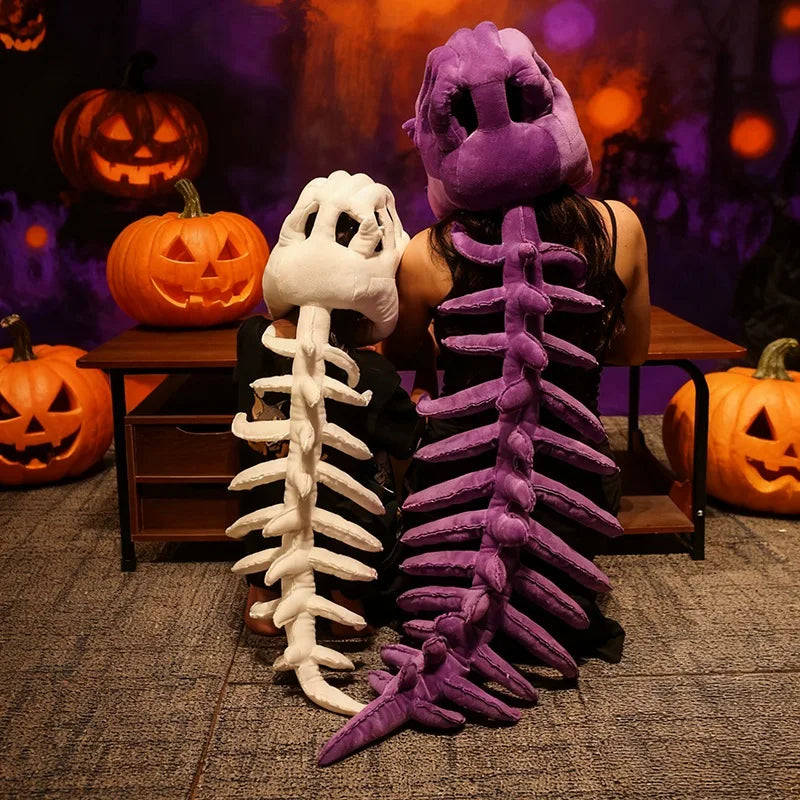 Un peluche squelette de dinosaure violet à côté d'un modèle squelette blanc dans un décor d'Halloween.