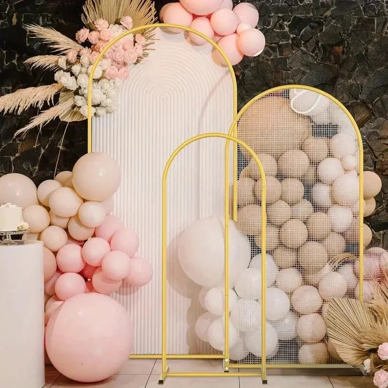 A display of pink and white balloons arranged on a gold metal arch stand against a dark stone background.