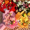 A bouquet of handmade crochet yarn flowers in various shades of pink, orange, and white, wrapped in colorful paper.