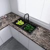 A black kitchen tray holds fresh green herbs and yellow lemons on a marble countertop near a window.