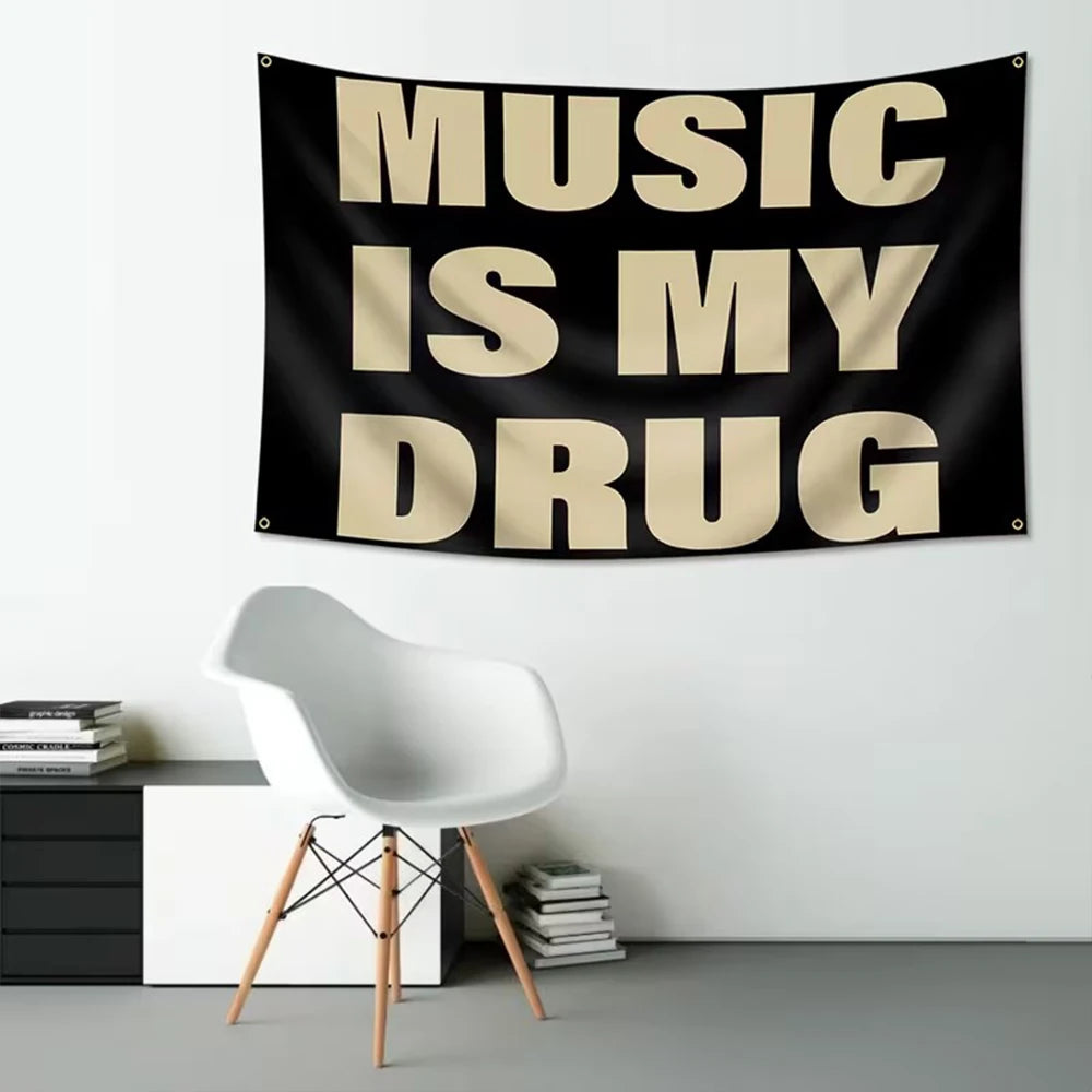 A black fabric tapestry with the text Music Is My Drug in large, cream-colored, sans-serif letters hanging on a white wall.