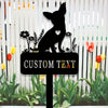 A black silhouette of a chihuahua dog with a heart on its chest is displayed on a garden stake surrounded by green plants.