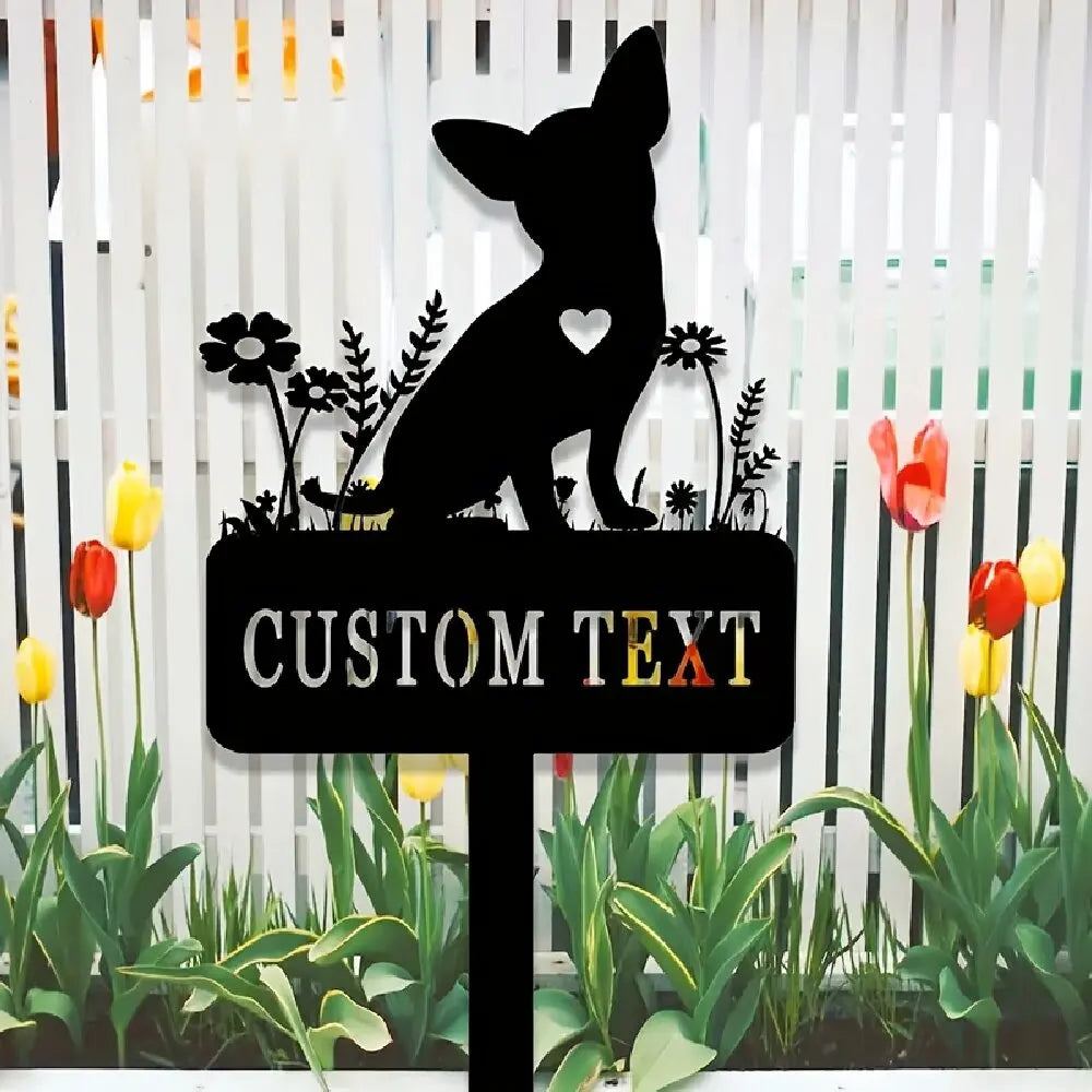 A black silhouette of a chihuahua dog with a heart on its chest is displayed on a garden stake surrounded by green plants.