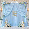 A light blue fabric backdrop with draped curtains and floral greenery for an event setting.