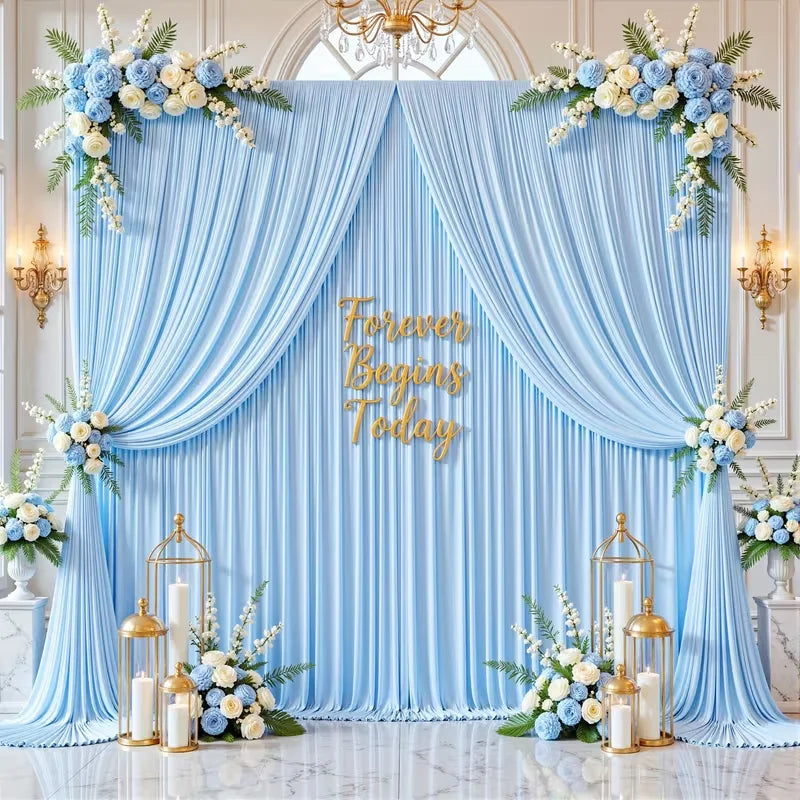 A light blue fabric backdrop with draped curtains and floral greenery for an event setting.