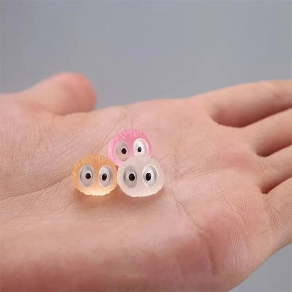 Three glow-in-the-dark resin ghost tree elves in pink and translucent colors resting on a hand.