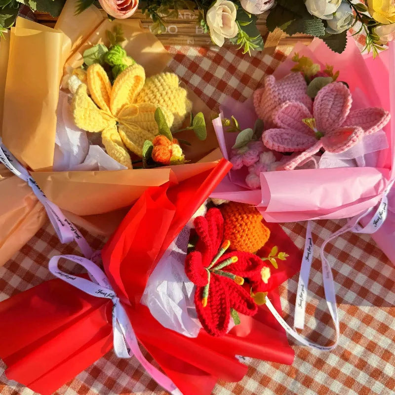 A bouquet of handmade crochet yarn flowers in yellow, pink, and red are displayed in tissue paper.