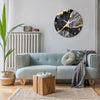A modern marble textured glass wall clock with gold accents hangs on a light gray wall above a light blue sofa.