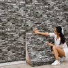 A young woman is installing self-adhesive 3D foam wall panels on a gray stone-look wall.