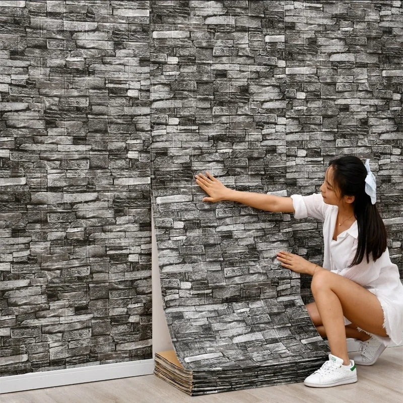 A young woman is installing self-adhesive 3D foam wall panels on a gray stone-look wall.