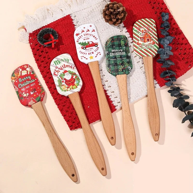 A set of festive Christmas silicone spatulas with wooden handles arranged on a red and white textured fabric.