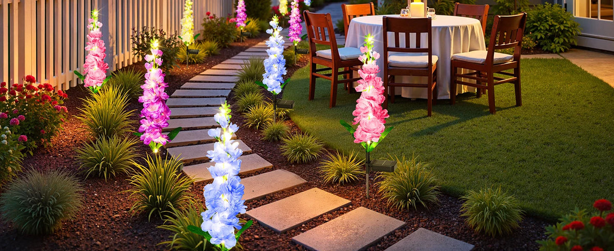 A garden pathway lined with pink and blue illuminated delphinium flower lights leading to a dining table.