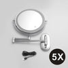 A round, silver-framed magnifying makeup mirror with a handle and USB charging cable.