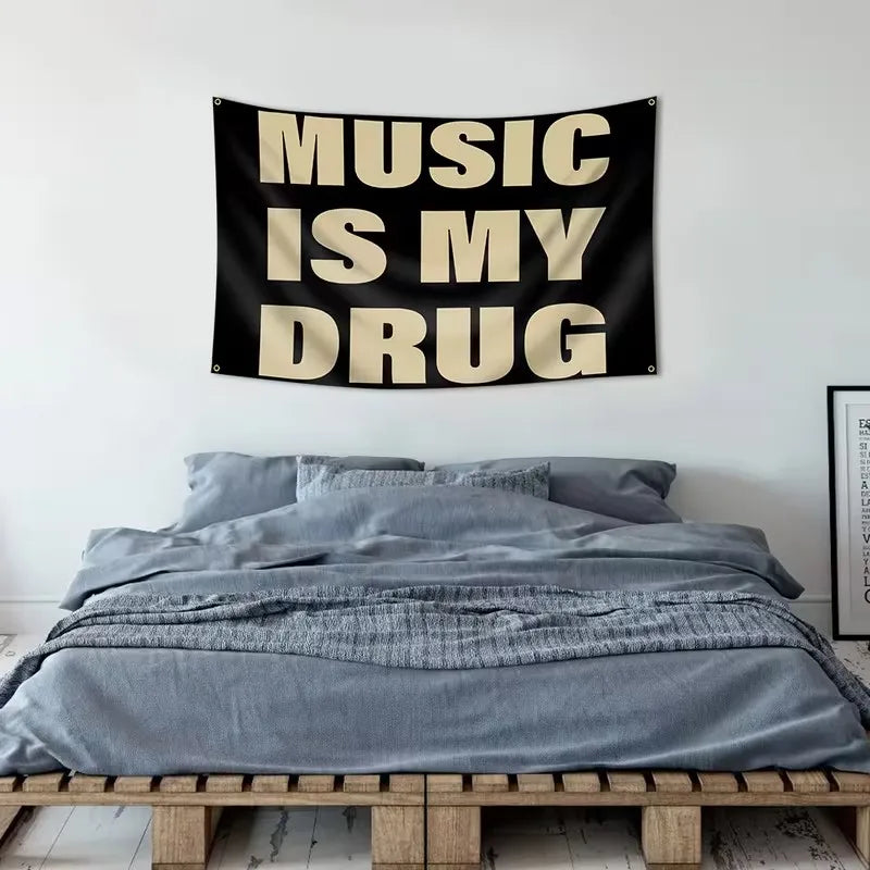 A black tapestry with the text Music Is My Drug in beige lettering hanging above a gray bed.