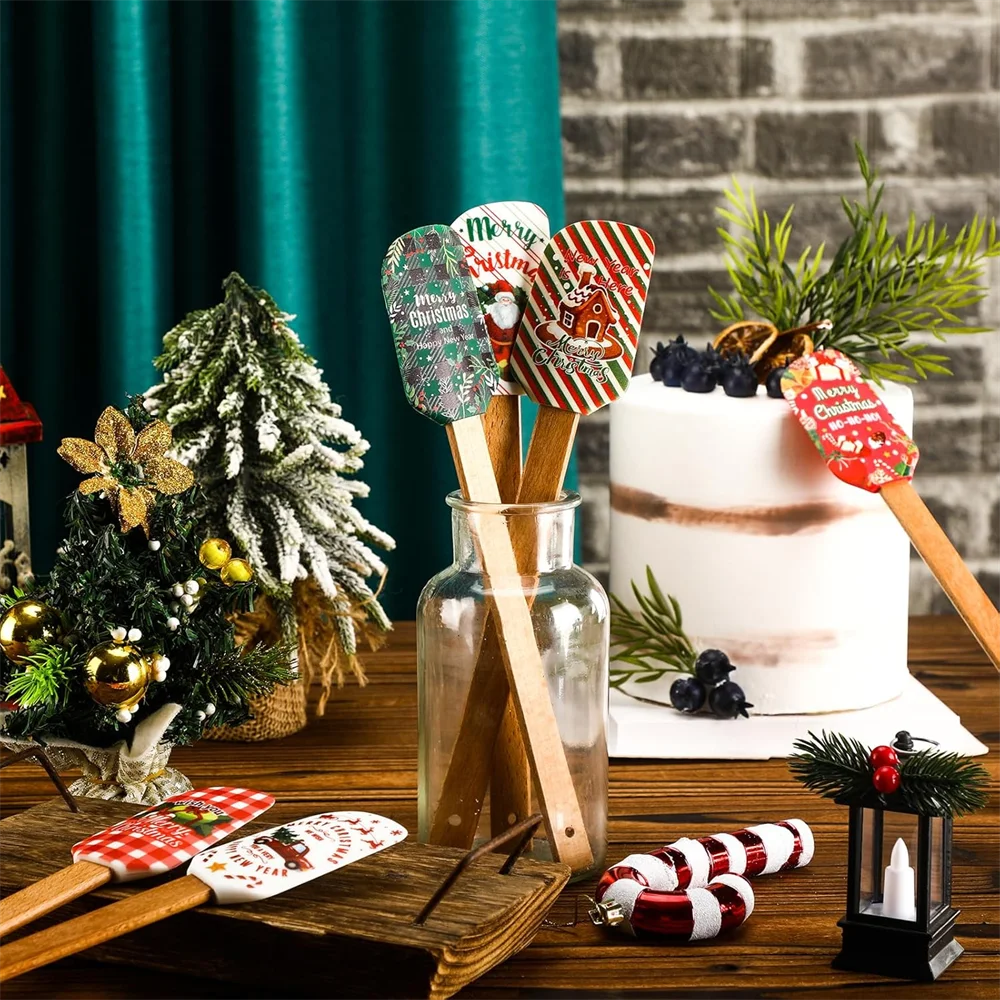 A festive Christmas silicone spatula with a wooden handle is displayed next to a decorated Christmas tree and a white cake.