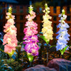 Four vertical stalks of colorful delphinium flowers illuminated by solar lights against a dark background.