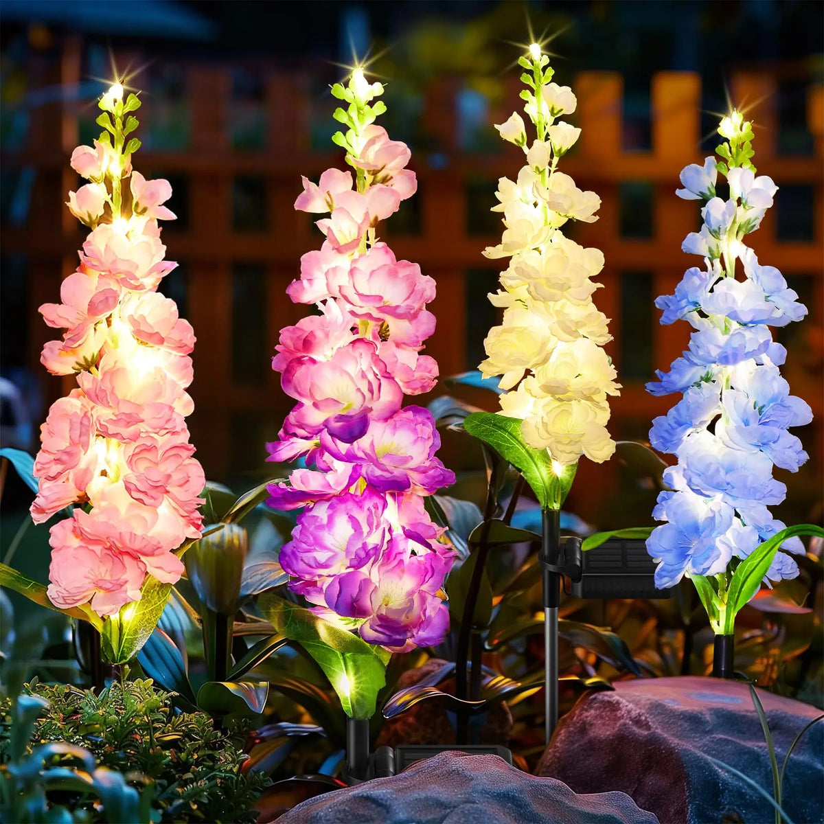 Four vertical stalks of colorful delphinium flowers illuminated by solar lights against a dark background.