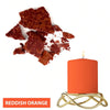 A reddish orange candle in a gold holder next to dried reddish orange dye blocks.