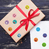 A brown gift box tied with a red ribbon decorated with colorful round smiling face stickers.