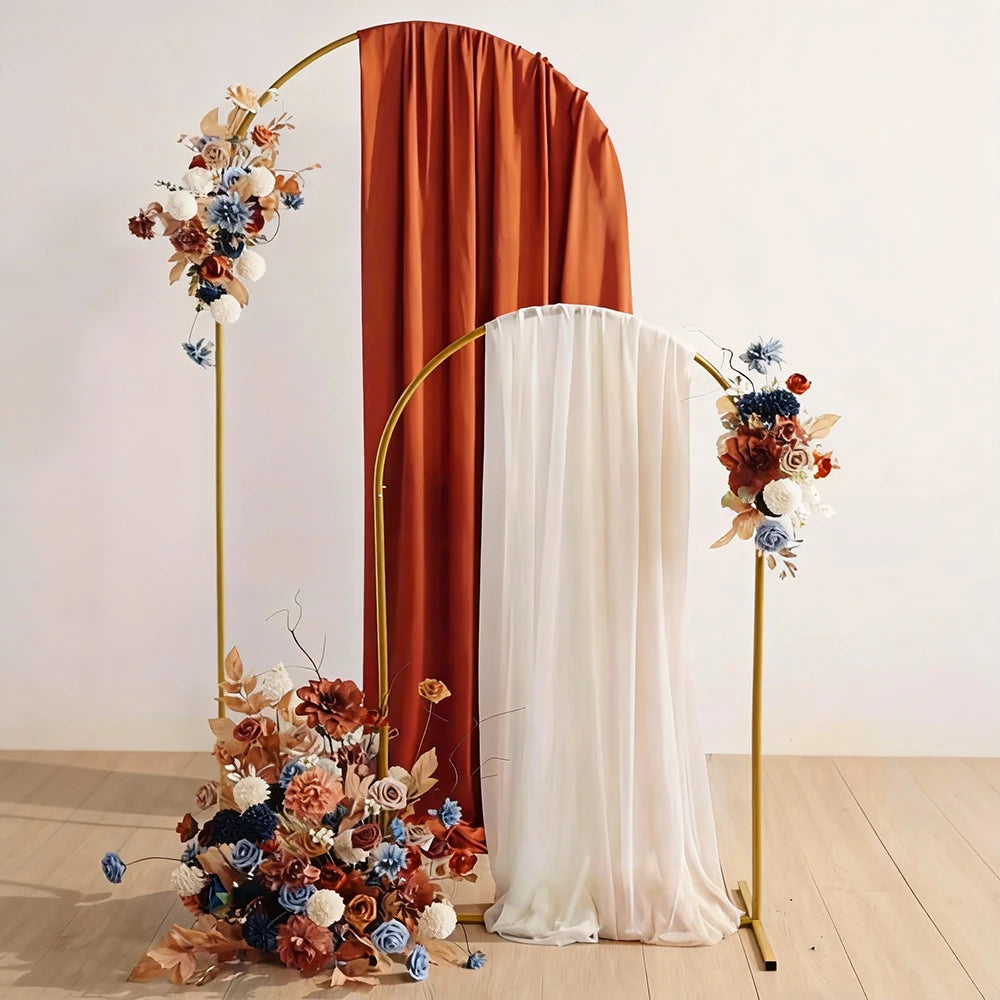 A gold metal arch stand decorated with dried flowers and draped white fabric.