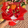 A bouquet of handmade crochet yarn flowers in orange and red are presented in red paper.