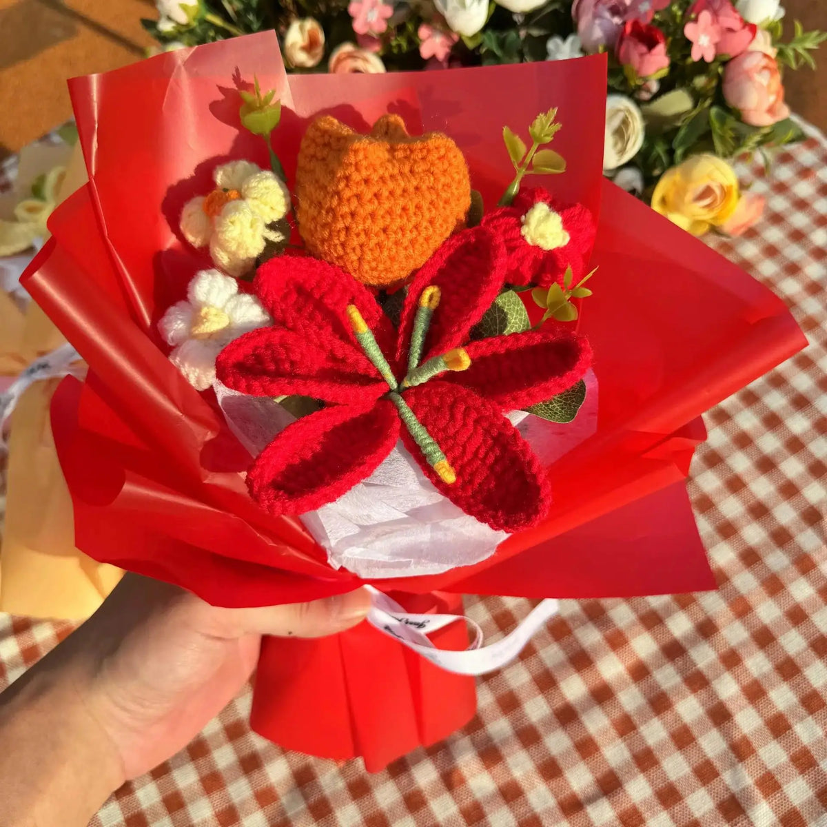 A bouquet of handmade crochet yarn flowers in orange and red are presented in red paper.