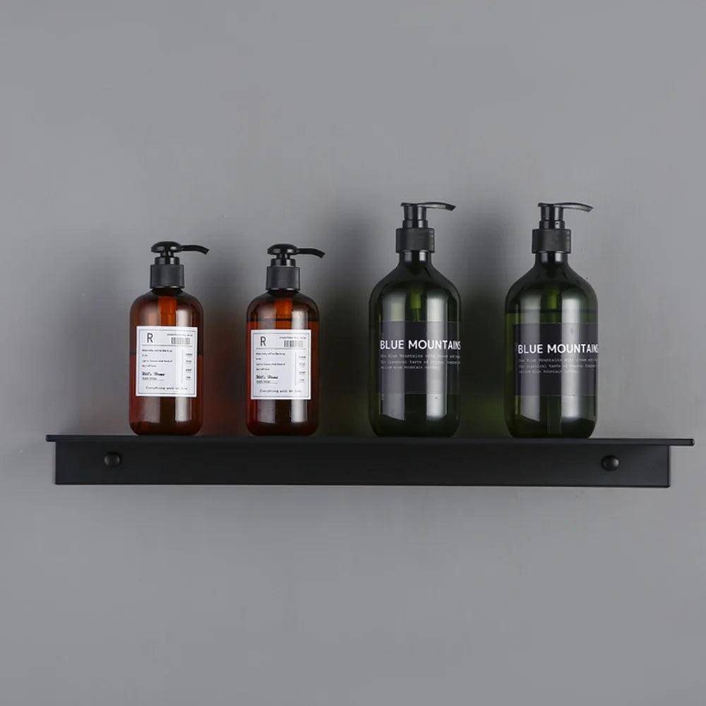 Three dark glass bottles of liquid soap or lotion displayed on a modern matte black wall shelf.