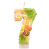 A yellow birthday candle shaped like the number 10, decorated with glitter and green moss.