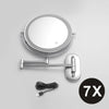 A round, silver-framed magnifying makeup mirror with a handle and USB charging cable.