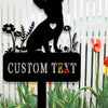 A black silhouette of a dog sits on a garden stake with custom text, surrounded by various plants.