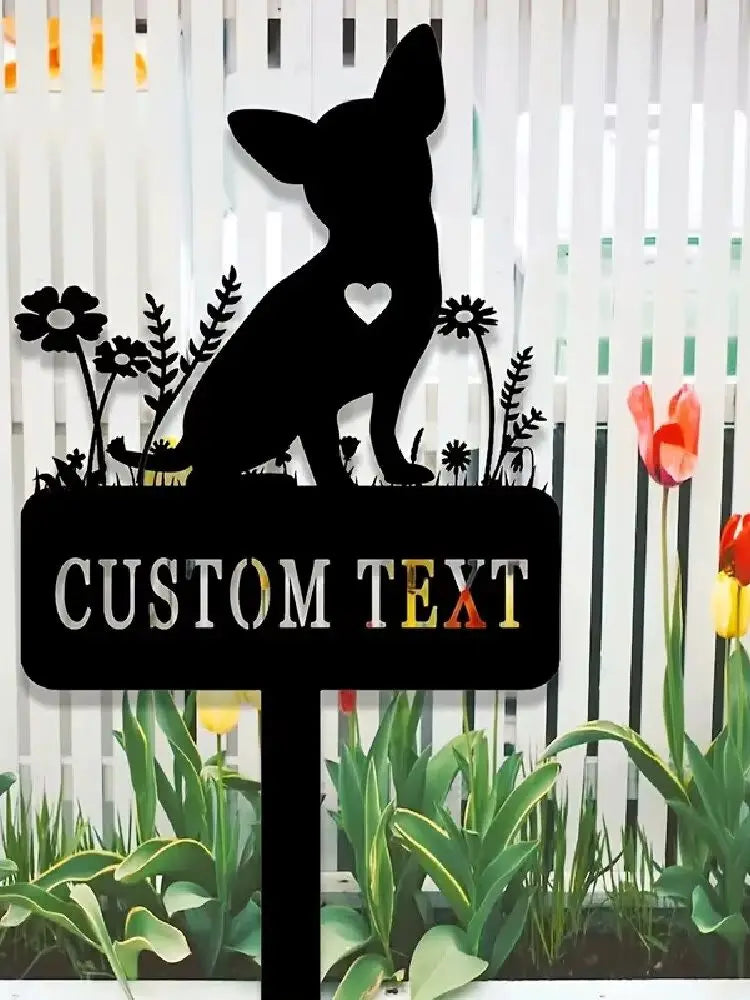 A black silhouette of a dog sits on a garden stake with custom text, surrounded by various plants.