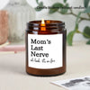 A dark glass candle jar with a lit candle and a white label sticker that reads Mom's Last Nerve oh look it's on fire