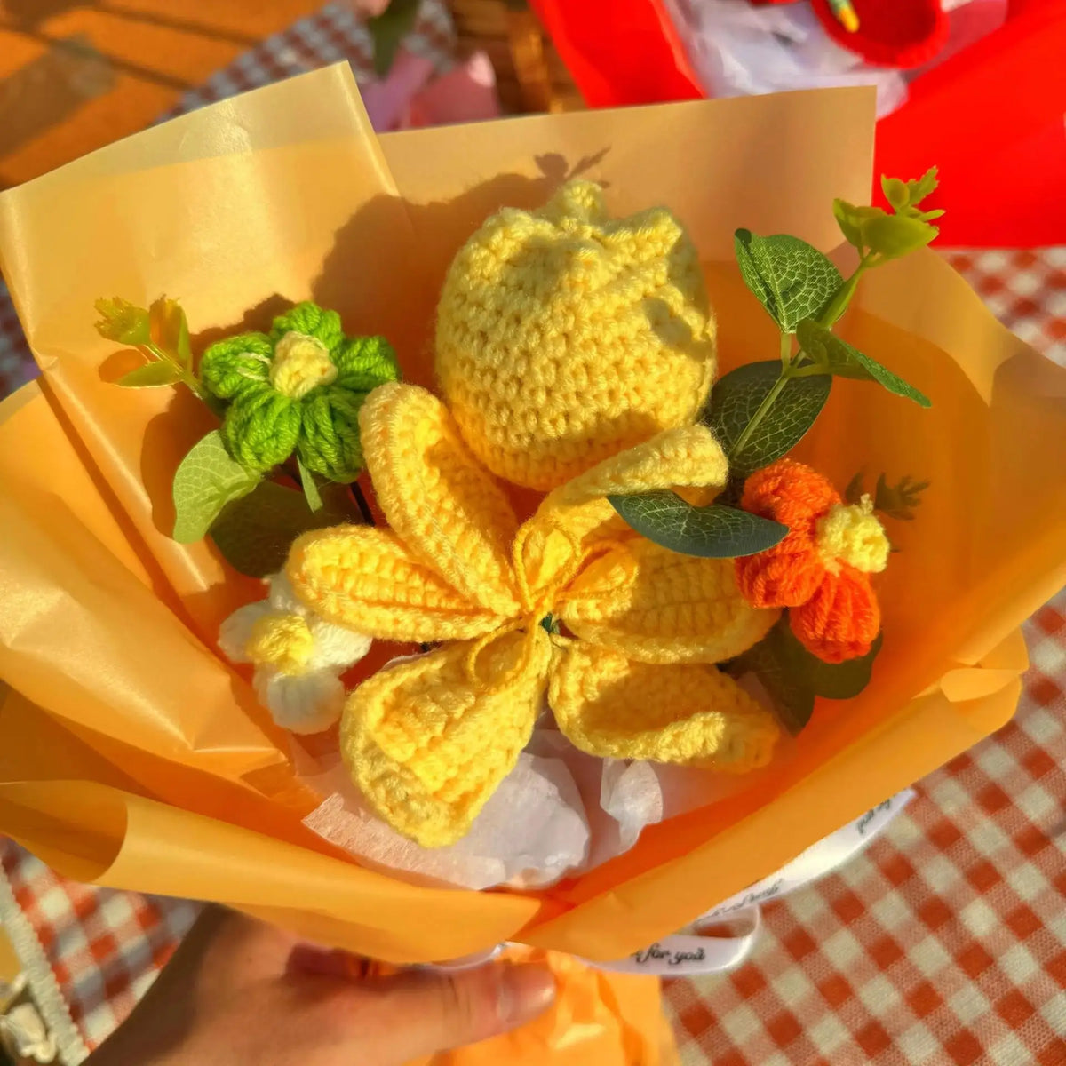 A bouquet of handmade crochet yarn flowers in yellow and orange nestled in an orange paper wrapper.