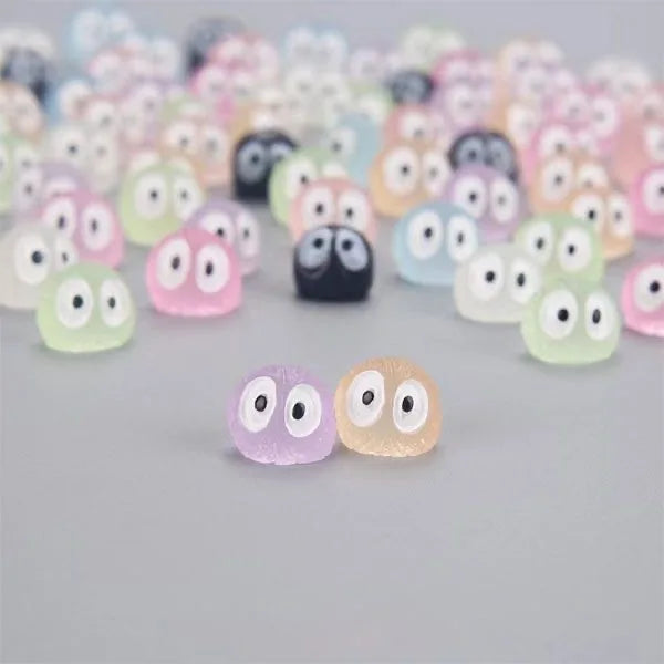 A collection of glow-in-the-dark resin ghost tree elves in various pastel colors arranged on a gray surface.