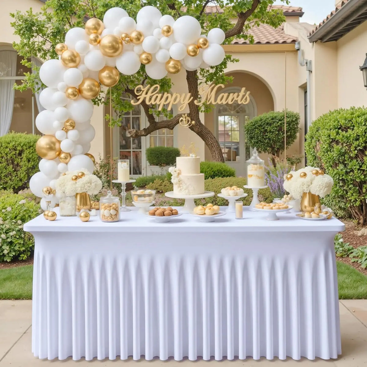 A white table covered with a pleated tablecloth displaying various desserts and a tiered cake in an outdoor setting.