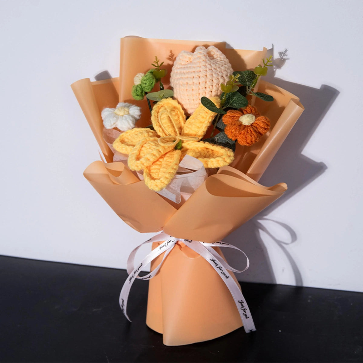A bouquet of handmade crochet yarn flowers in shades of yellow and orange presented in a kraft paper holder.